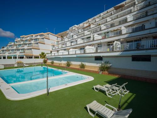 a large apartment building with a swimming pool and two chairs at Incredible Sunsets in Puerto Rico de Gran Canaria