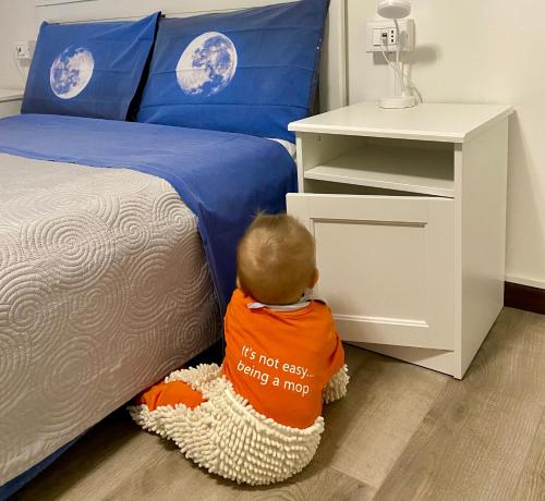 a baby sitting on the floor next to a bed at Appartamento “Del TuF” in Sondrio Centro in Sondrio