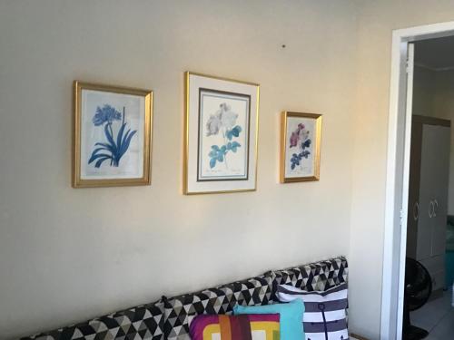 four framed pictures on a white wall with a couch at Quitieenete Arraial do Cabo in Arraial do Cabo
