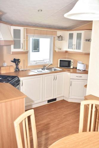 una cucina con armadi bianchi, lavandino e finestra di Caprice Gold SU18 a Minehead