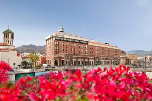 un gran edificio de ladrillo con flores rojas delante de él en NH Málaga, en Málaga