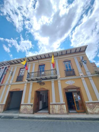 un edificio amarillo con banderas en la parte delantera en Hotel Coronel, en Cuenca