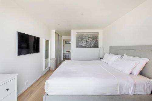 a white bedroom with a large bed and a flat screen tv at Aloft at Era with Sweeping Balcony Views in Melbourne
