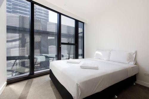 a white bed in a room with a large window at The Claremont - Refined Resort Style Living in Melbourne