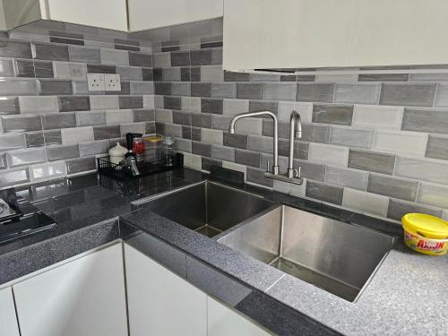 uma cozinha com um lavatório de aço inoxidável e azulejos cinzentos em TSK Homestay Taman Sri Kluang em Keluang