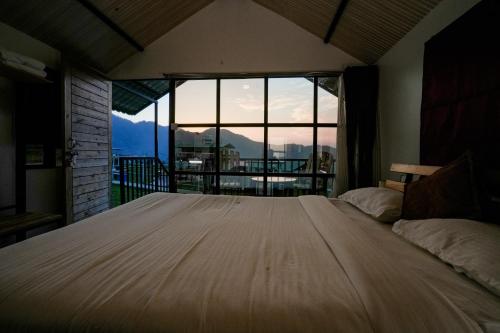 a large bed in a room with a large window at The Hillside Cottages in Kanatal