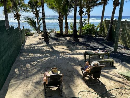 Dos personas sentadas en sillas en la playa en ShineAwayHomes -AC Beachfront RAROTONGA, en Matavera