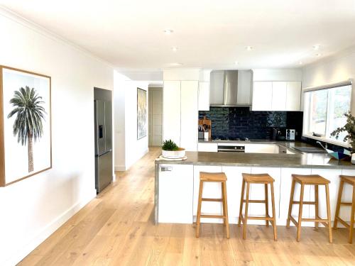 a kitchen with white cabinets and a island with bar stools at Coastal Family Haven with Pool - Mornington Peninsula in Frankston South