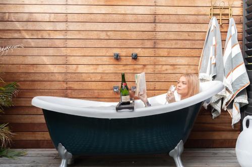a woman sitting in a bath tub with a bottle of wine at Maggies The Little Black Cottage - Hunter Valley in Cessnock