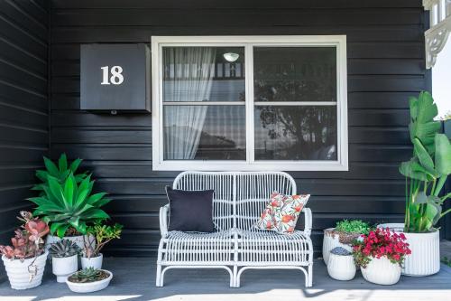 a white chair with pillows on a porch with plants at Maggies The Little Black Cottage - Hunter Valley in Cessnock