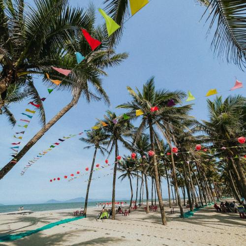 a beach with palm trees and kites flying in the sky at Cocohut Hoi An Homestay in Hoi An