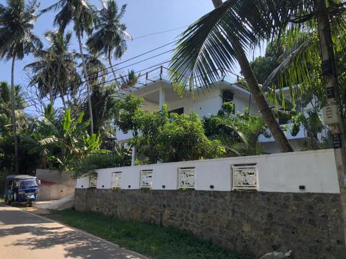 a house behind a stone wall with palm trees at Divya Sea View in Dodampahala East