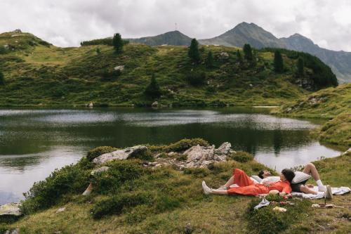 two people laying on the grass next to a lake at Hotel Steiner Superior in Obertauern