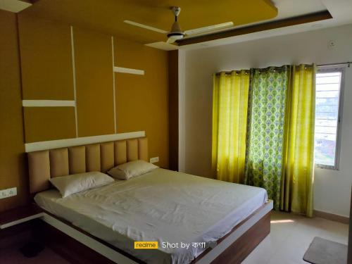 a bedroom with a bed and a window with yellow curtains at Mayer Anchal in Bāghdogra