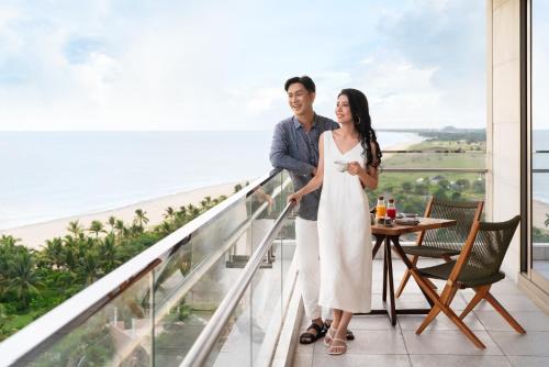 a couple standing on a balcony with the ocean in the background at New World Hoiana Beach Resort in Hoi An