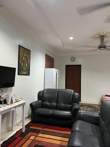 sala de estar con sofá de cuero negro y TV en Tok Wan Roomstay en Kampong Banggol Binjai