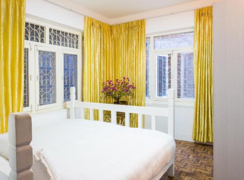 a bedroom with a white bed and yellow curtains at The Global Nomad Apt Centrally Located in Kathmandu