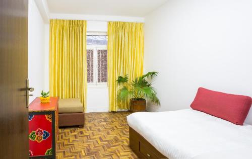 a bedroom with a bed and a window with yellow curtains at The Global Nomad Apt Centrally Located in Kathmandu