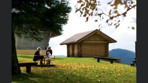 dos mujeres y un niño sentados en un banco frente a una cabaña en Brunarica Macesen Smogavc, en Zreče