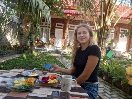 una mujer sentada en una mesa con un plato de fruta en TelukBiru Homestay, en Banyuwangi