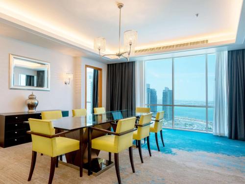 a dining room with a glass table and yellow chairs at Hilton Doha in Doha