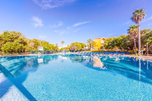 una gran piscina con sillas azules y palmeras en Vibra Blanc Palace Aparthotel, en Sa Caleta