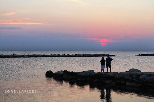 a couple standing on the rocks in the water at sunset at Residence Rimini Relax in Rimini