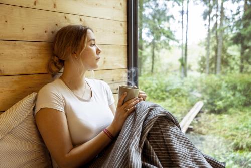 a woman looking out a window while holding a cell phone at Chic Sauna Cabin Near the Sea - KOHIN Cabin Nº02 in Tsitre