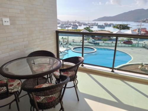 balcón con mesa, sillas y vistas a la piscina en Frente mar 3 quartos Praia dos Anjos Residence, en Arraial do Cabo