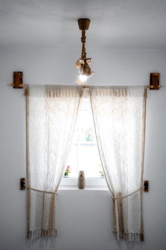 a window with white curtains and a chandelier at Kata Kulcsosház in Odorheiu Secuiesc