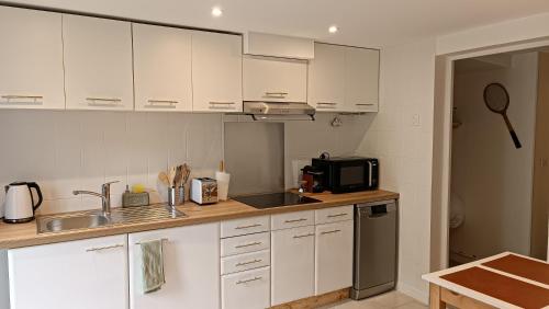 une cuisine avec des armoires blanches, un évier et un micro-ondes dans l'établissement Refuge des Myosotis - proche Chambéry - jardin - calme - cosy, à Barberaz