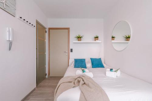 een witte slaapkamer met een bed met blauwe kussens en een spiegel bij Moderne lichtrijke studio vlakbij strand en casino Middelkerke in Middelkerke