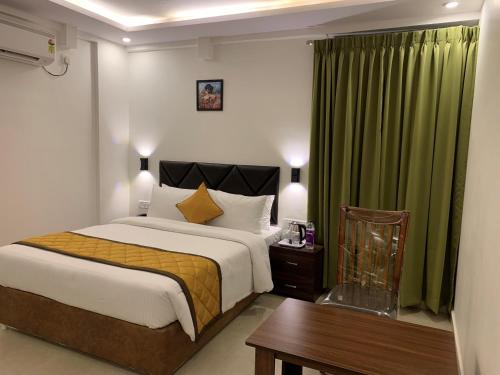 a bedroom with a bed and a table and green curtains at Hotel Le Grandeur in Bangalore