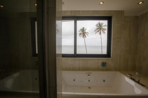a bathroom with a tub and a window with palm trees at Cowork Lab Suites in Maputo