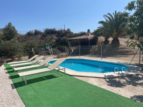 una piscina con 2 tumbonas y un césped verde en Casa Ramoncico. Finca el Campillo en Blanca