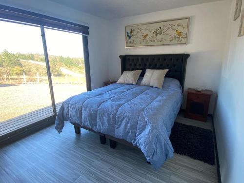 a bedroom with a bed with a blue blanket and a window at Ecobosque y cabañas in Paredones