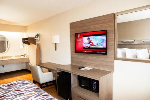 a hotel room with a bed and a tv on a wall at Red Roof Inn Rochester - Henrietta in Henrietta