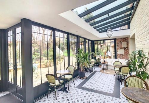 a conservatory with tables and chairs and windows at Les Glycines de Monchy- Chambres d'hôtes in Monchy-Humières