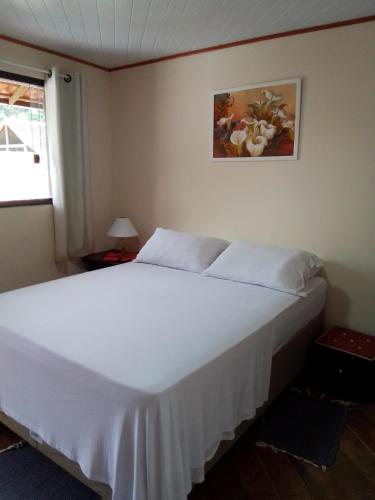 um quarto com uma cama branca e uma fotografia na parede em Hospedagem Frez em Nova Friburgo