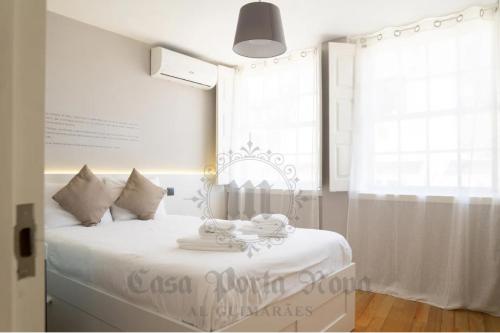 een witte slaapkamer met een bed met witte lakens en een raam bij Casa Porta Nova AL in Guimarães