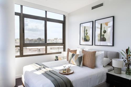 a white bedroom with a bed and two windows at Modern Elegance Caulfield North in Melbourne