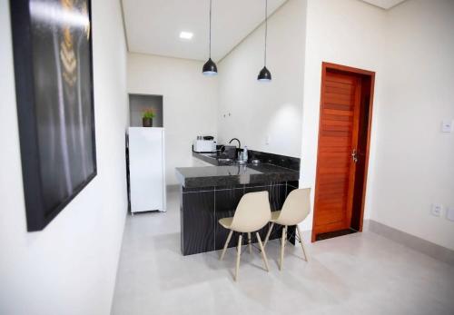 a kitchen with a black counter and two white chairs at Capuzzo Flat 1 in Redenção