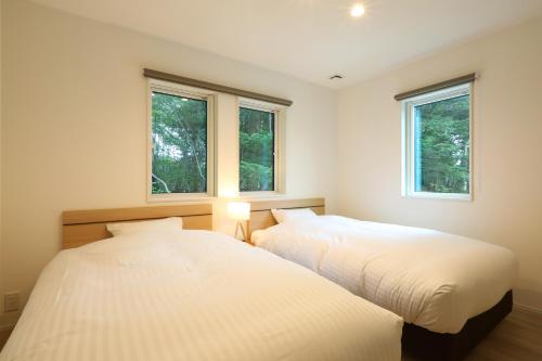 two beds in a bedroom with two windows at Albatross Karuizawa in Karuizawa
