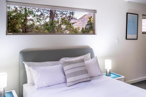 a bedroom with a white bed with a large window at Driftwood in Coles Bay