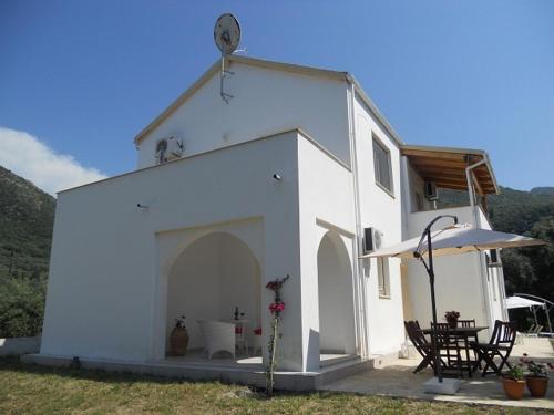 a white building with two chairs and an umbrella at Villa Fedrita in Acharavi