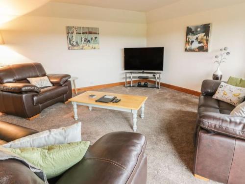 a living room with leather furniture and a flat screen tv at Middle Byre at Clauchan Holiday Cottages in Gatehouse of Fleet