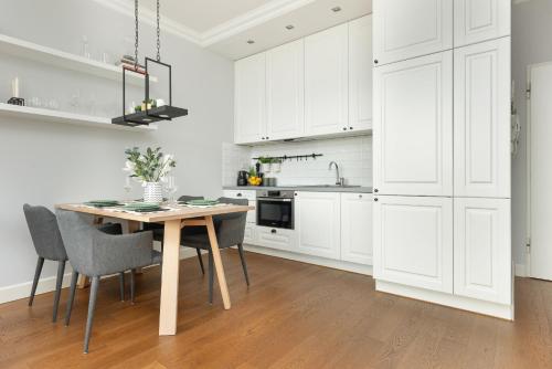a white kitchen with a wooden table and chairs at Cozy Apartment Gieysztora Wilanów by Renters in Warsaw