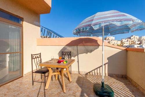 uma mesa e cadeiras com um guarda-sol numa varanda em Pool & Sea Merill Apartments Mellieha - Happy Rentals em Mellieħa