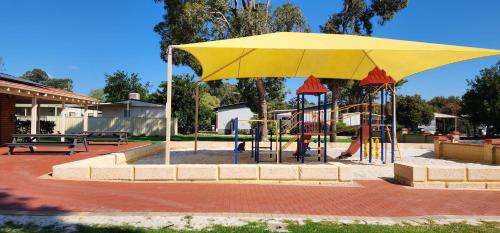 Banksia Tourist Park في بيرث: ملعب فيه مظله صفراء في حديقه