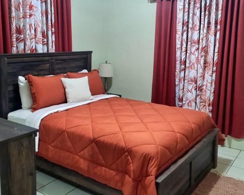 a bedroom with a bed with an orange comforter and red curtains at Tropix Getaway - rental car available in Crocus Hill
